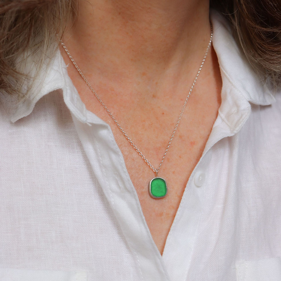 Bright green sea glass and silver pendant necklace on a white woman wearing a cream linen shirt