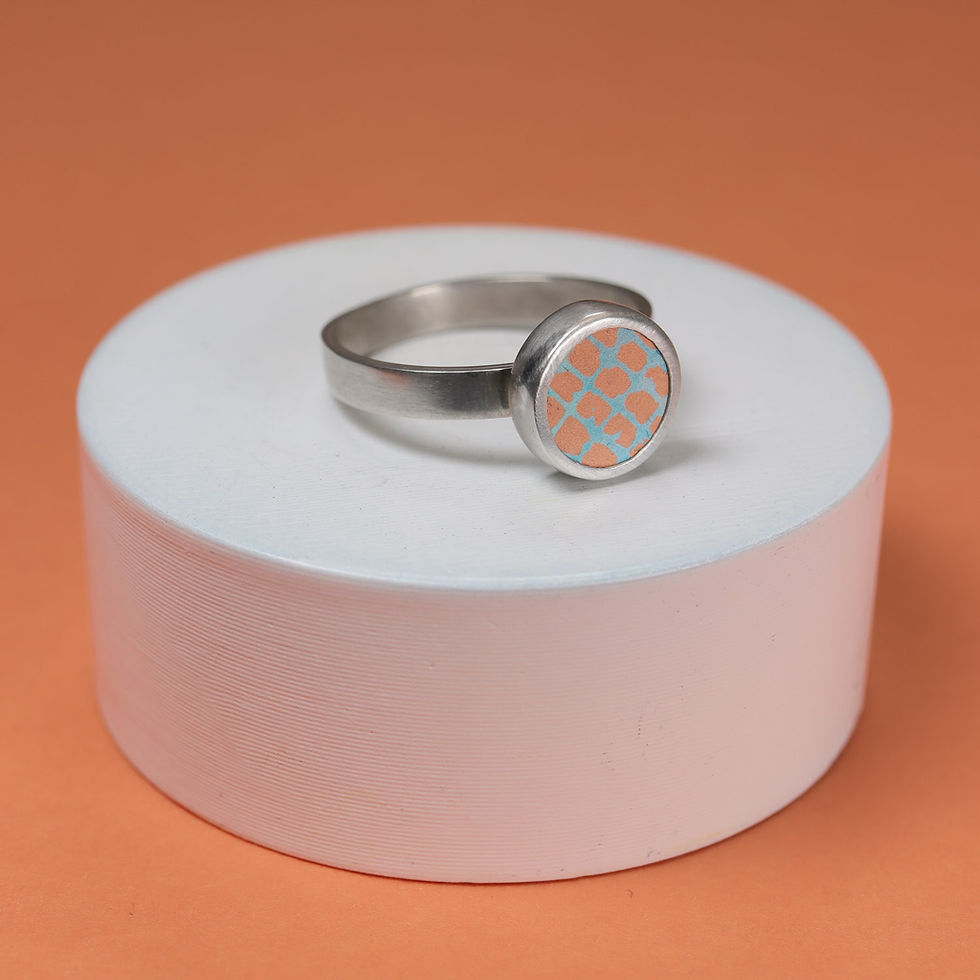Orange and turquoise blue aluminium silver ring on a white plinth with orange background