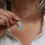 Thumbnail: Light aqua blue aluminium tear drop and red sea glass silver cluster necklace on white woman wearing a cream linen shirt