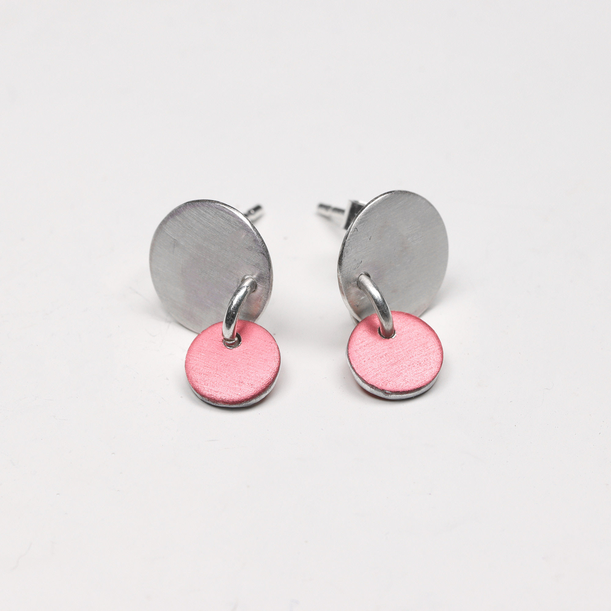 Dusky pink anodised aluminium and silver drop stud earrings on a white background