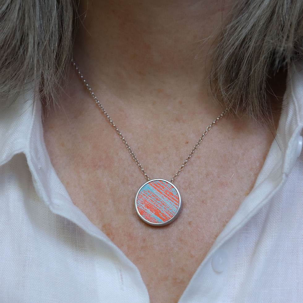 Thumbnail: Orange and turquoise aluminium and silver round pendant necklace on a white woman wearing a cream linen shirt