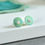 Thumbnail: Green and turquoise round silver stud earrings on white and grey slap with green and blue material behind