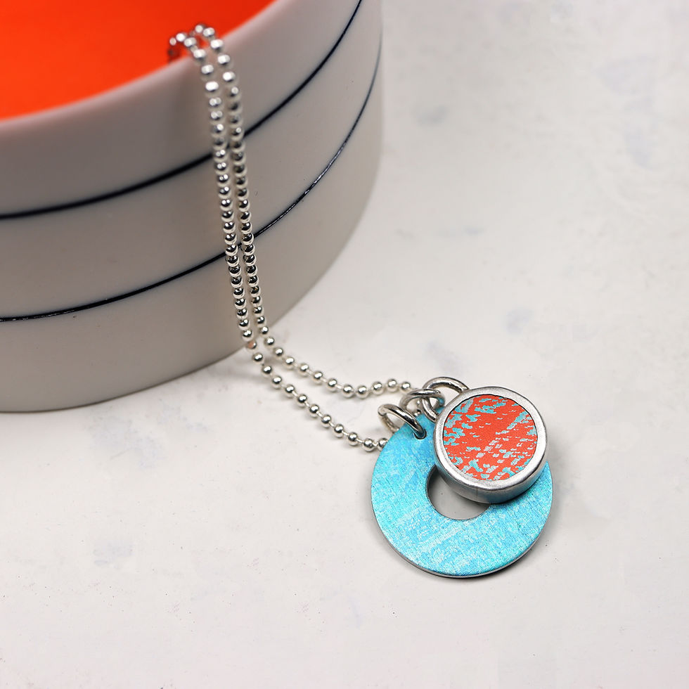 Thumbnail: Turquoise and orange silver necklace on a white background with a white dish with orange centre