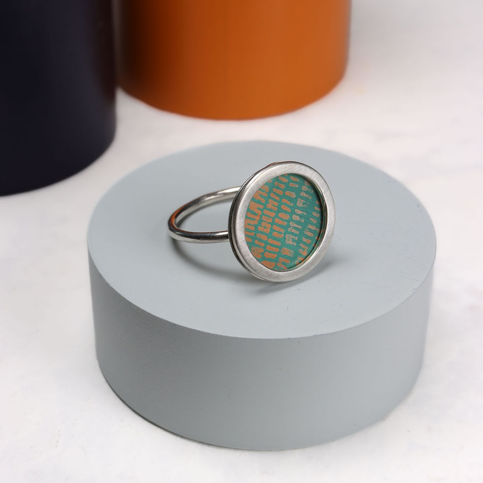 Green and orange anodised aluminium and silver ring on grey display plinth