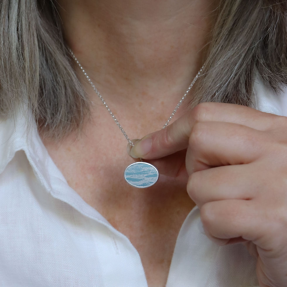 Thumbnail: Blue sky cloud aluminium and silver oval pendant necklace on a white woman wearing a cream linen shirt
