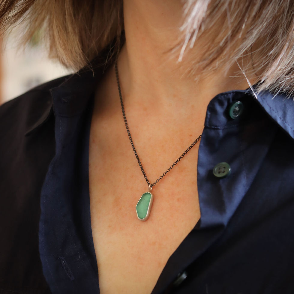 Thumbnail: Light aqua blue sea glass and oxidised silver pendant necklace on a white woman wearing a dark blue shirt