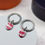 Thumbnail: Red and silver oval drop earrings on grey plinth with orange and blue plinth in background