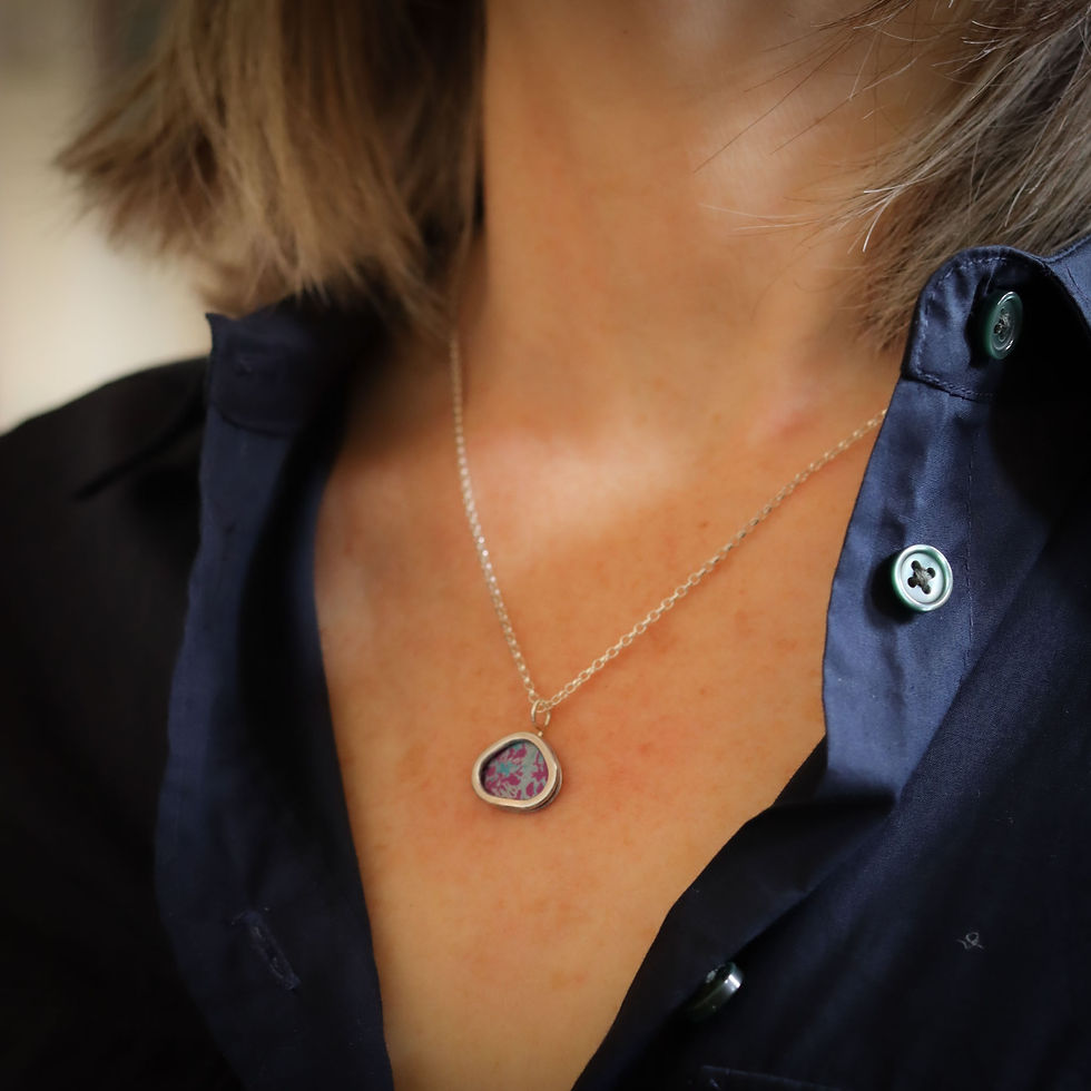 Thumbnail: Magenta pink and blue triangular silver pendant necklace on a white woman wearing a dark blue shirt