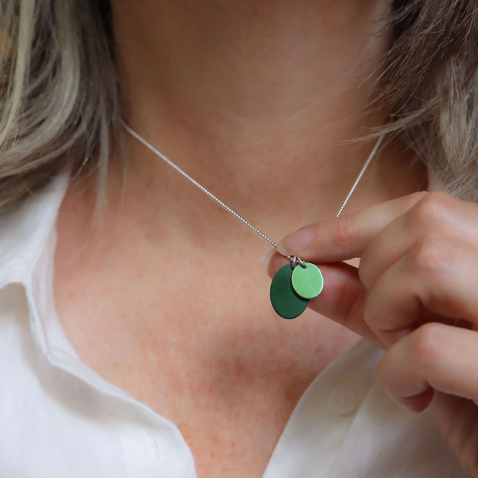 Thumbnail: Dark and light green anodised aluminium ovals silver necklace on a white woman wearing a cream linen shirt