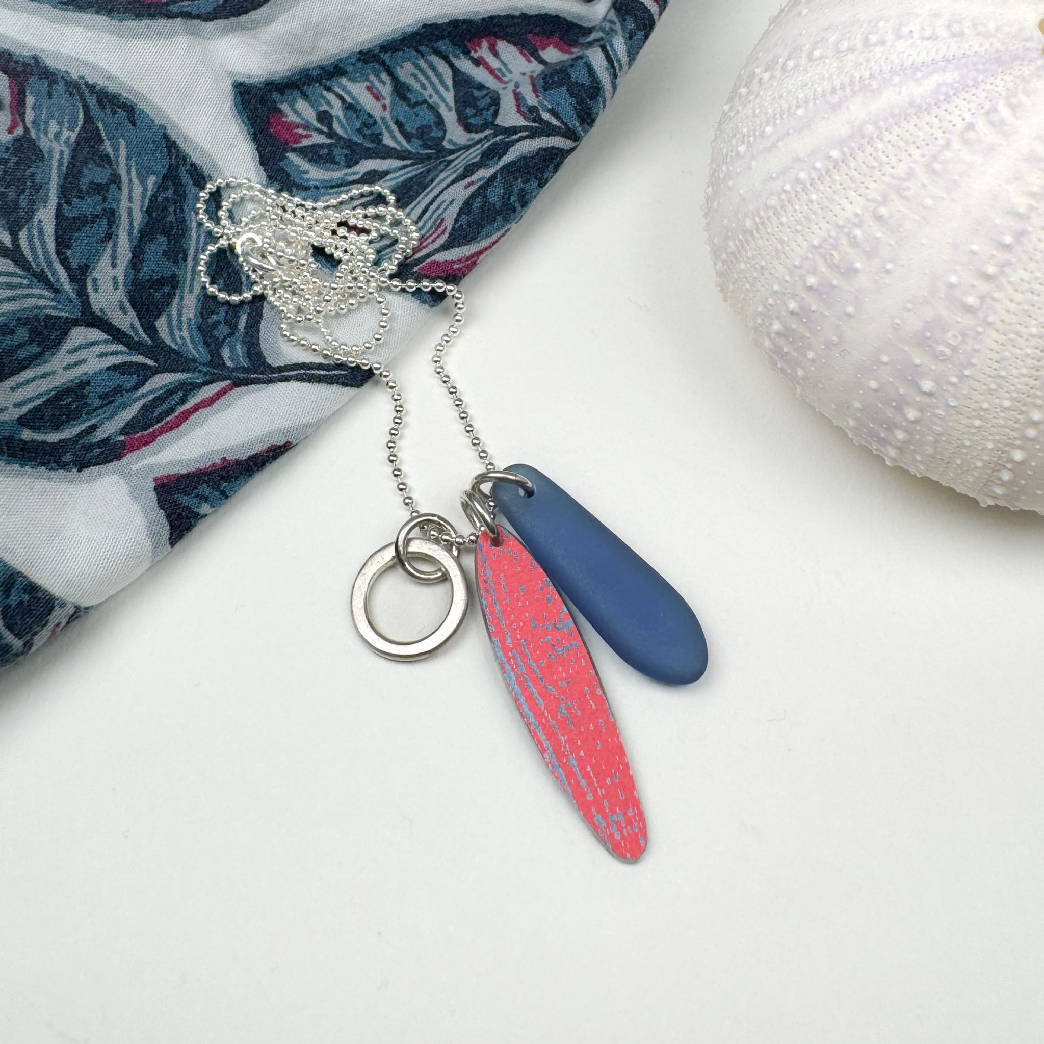 Raspberry red and blue cultured sea glass silver cluster necklace on a white background with matching shirt and sea urchin