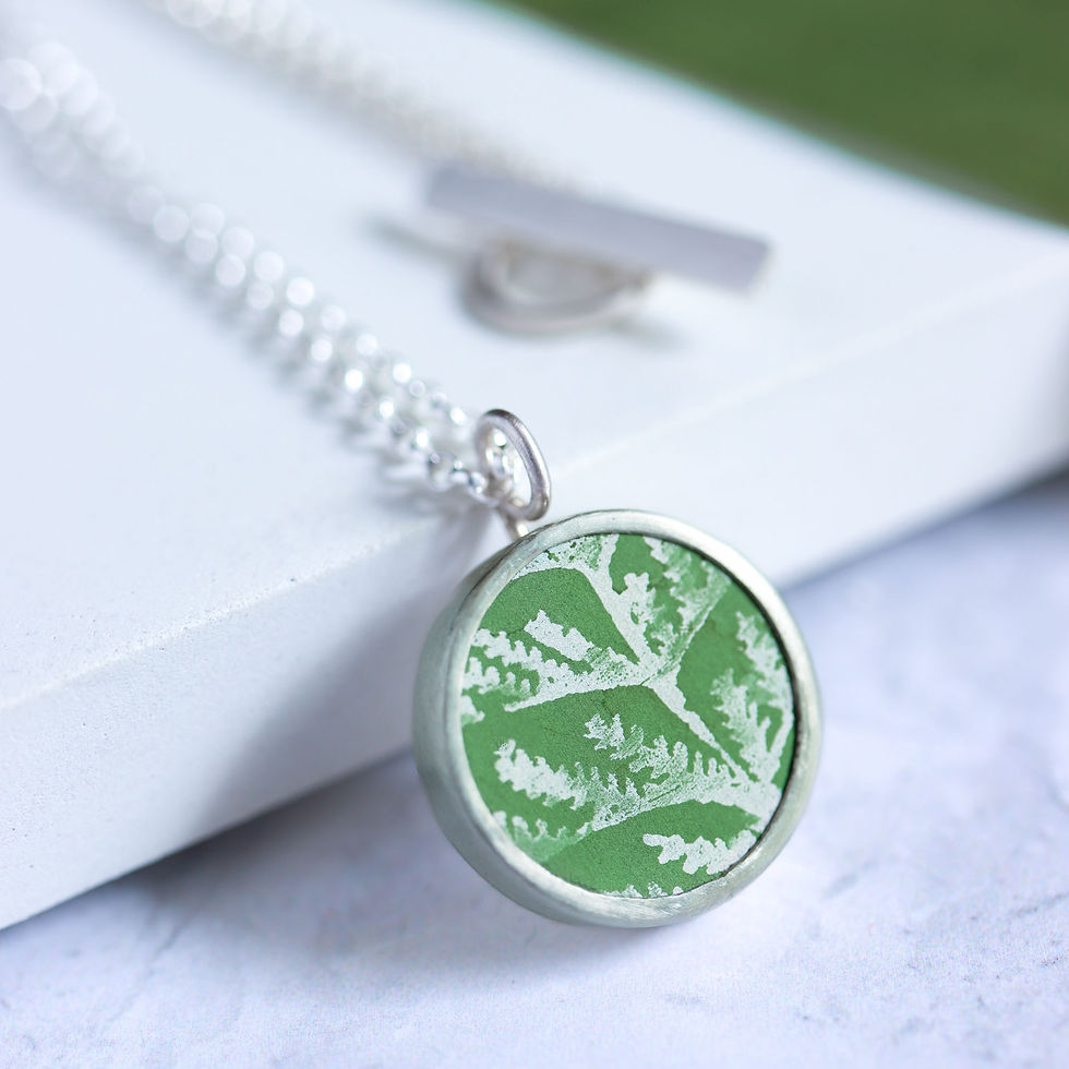 Thumbnail: Green leaf patterned aluminium and silver pendant necklace on a white block with ribbon
