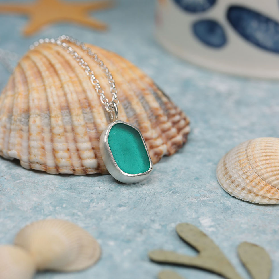 Teal green sea glass and silver pendant necklace on a shell on a blue background
