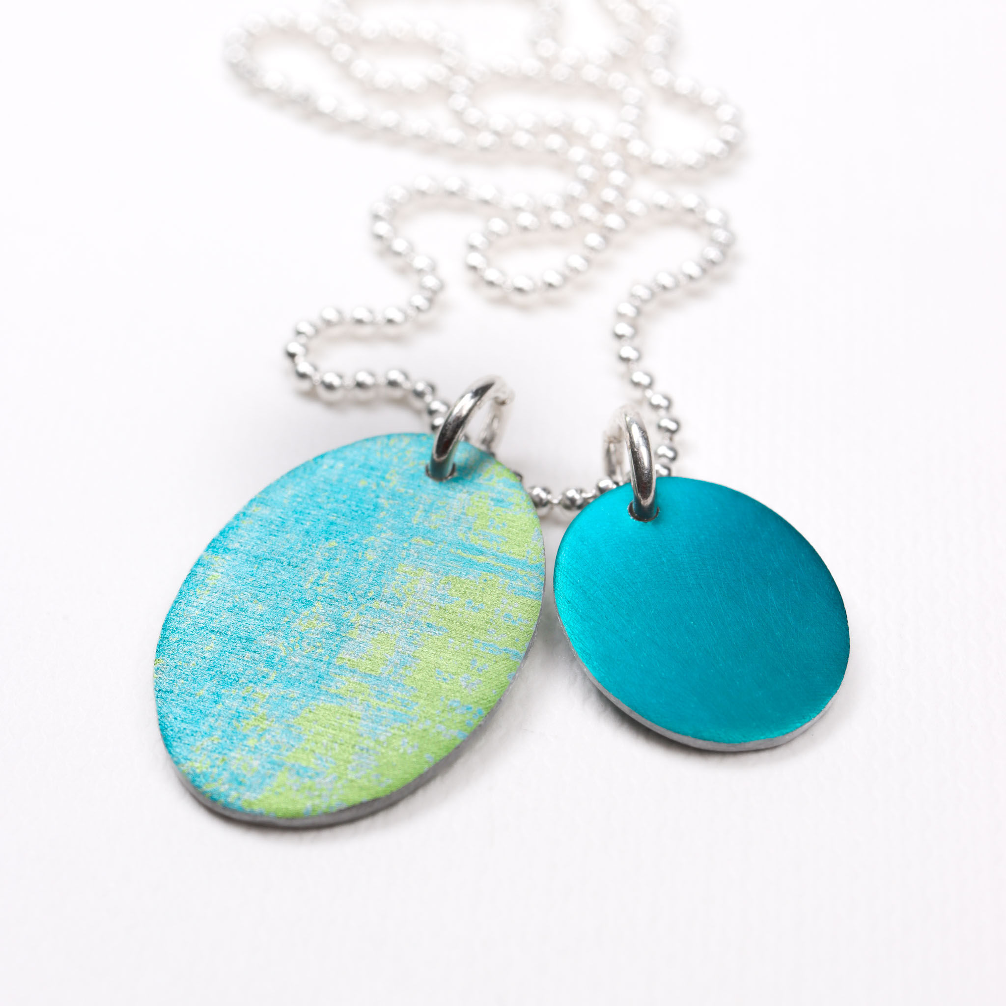 Turquoise blue and teal green oval aluminium cluster necklace on a white background