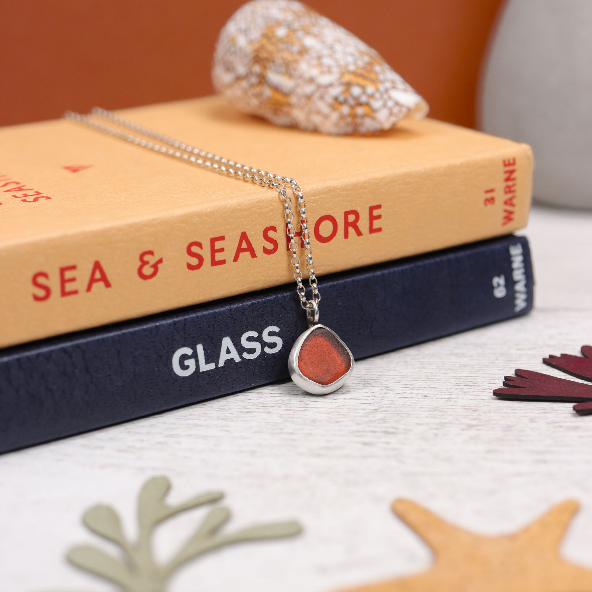 Dark orange sea glass and silver pendant necklace on observer books of sea and glass