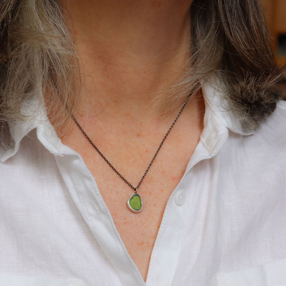 Green sea glass and silver pendant necklace on a white woman wearing a cream linen shirt