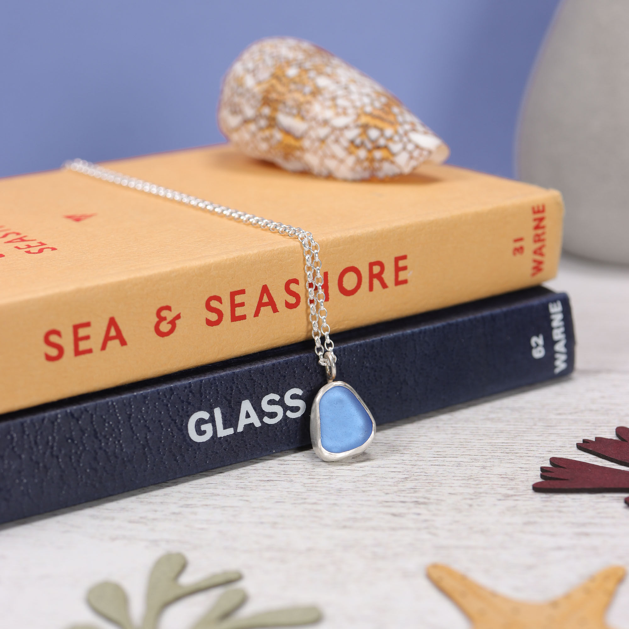 Violet blue sea glass and silver minimalist pendant necklace with observer bookson a white background