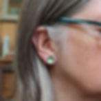 Green aluminium and silver stud earrings on a white woman
