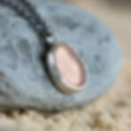 Blush pink sea glass and silver pendant necklace on a rock on a sandy beach