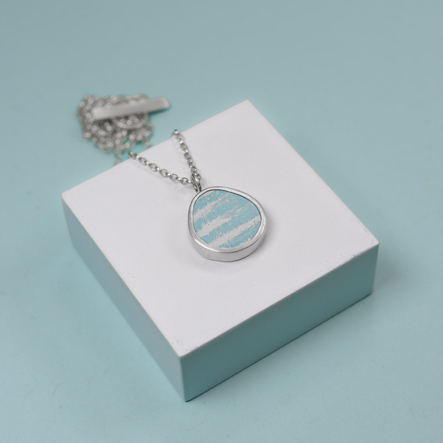 Duck egg blue tear drop anodised aluminium and silver pendant necklace on a blue background