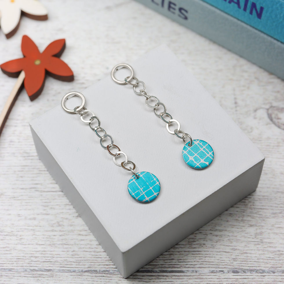 Turquoise blue cross hatch silver chain dangly earrings on a plinth with observer books behind