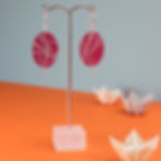 Large magenta pink red and silver oval earrings on an earring stand on an orange background