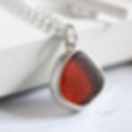 Thumbnail: Dark orange sea glass and silver pendant necklace leaning against a white block