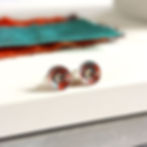 Orange and turquoise aluminium and silver interchangeable stud earrings on a white slab with ribbons behind