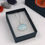 Thumbnail: Blue sky cloud aluminium and silver oval pendant necklace in an open jewellery box  on a white background