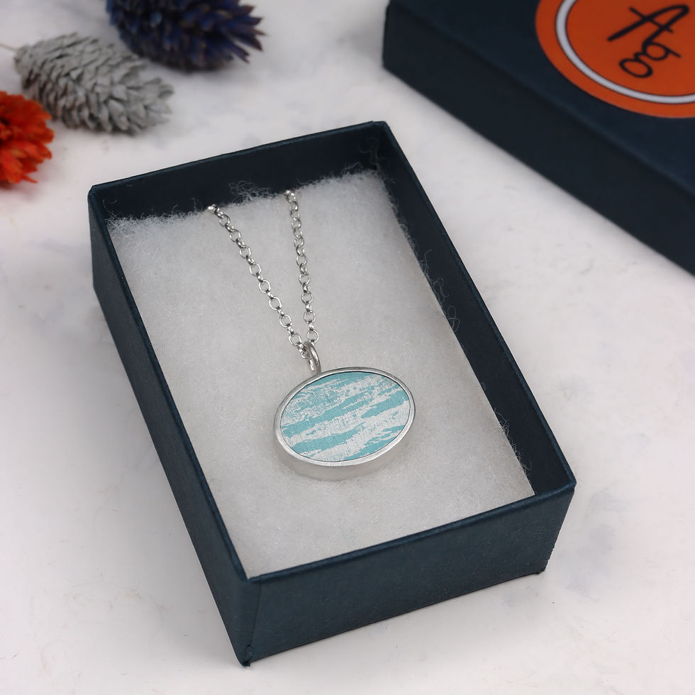 Thumbnail: Blue sky cloud aluminium and silver oval pendant necklace in an open jewellery box  on a white background