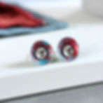 Red and turquoise aluminium and silver interchangeable stud earrings on a white and grey block with matching material behind