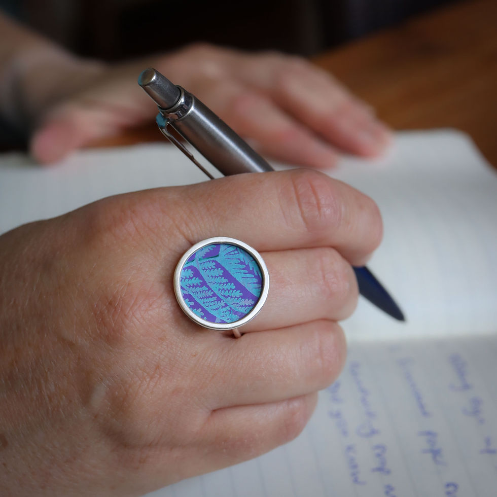 Purple and turquoise aluminium and silver rivet ring on a white woman with pen and notebook