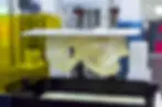 3D printer creating a translucent object. Yellow enclosure in the background, with a mechanical, industrial setting.
