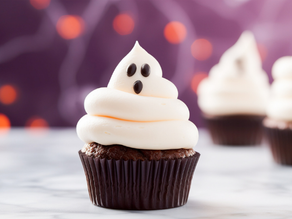 Ghost-themed cupcake with chocolate eyes, white frosting swirl, on a marble surface. Blurred purple background with orange bokeh lights.