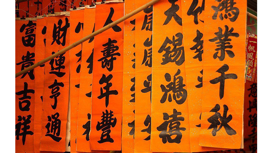Orange banners with bold black Chinese calligraphy hang closely, creating a vibrant display. The setting appears festive and cultural.