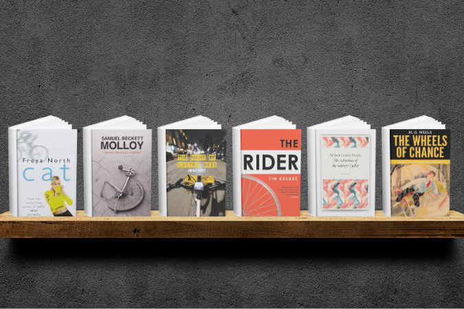 Books on a wooden shelf with varied cover designs: a yellow cat, a bicycle wheel, night city traffic, orange bike wheel, abstract art, and retro cycling.