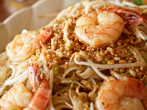 A plate of shrimp pad thai with the focus on cooked shrimp, bean sprouts, and crushed peanuts. Warm tones create a delicious, inviting feel.