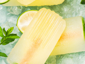Yellow popsicles with lime slices on crushed ice. Fresh mint leaves beside the icy treats create a refreshing summer vibe.