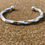 Thumbnail: Twisted sterling silver torque bangle for men photographed on sand