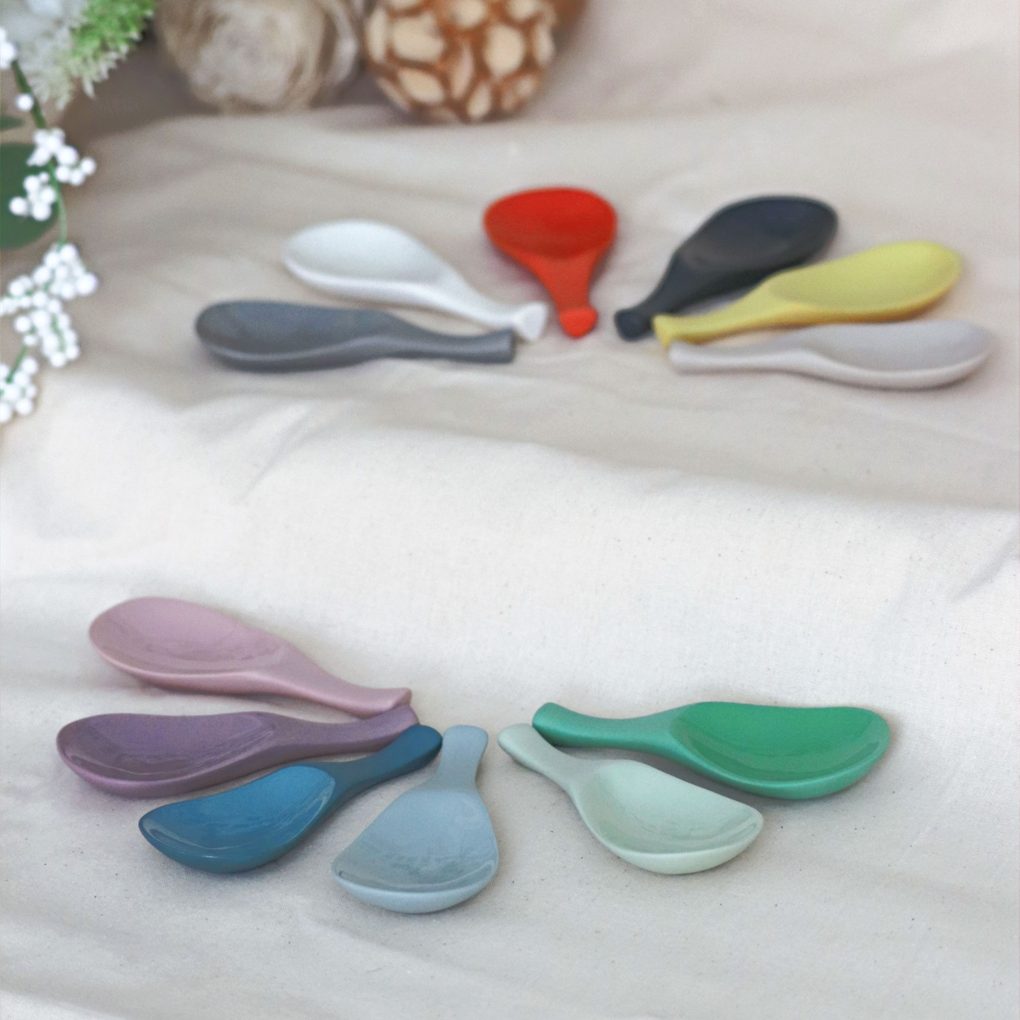 Twelve colourful ceramic spoon rests sit on a cream table cloth