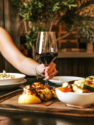 hand holding red wine glass on table with other mediterranean dishes with tree in the backgroud