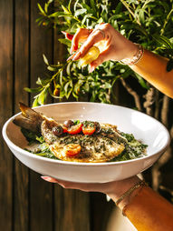 hand squeezing lemon on a branzino dish