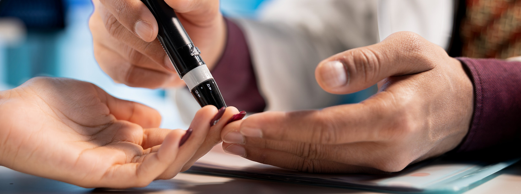 Close-up of a healthcare professional performing a diabetes finger-prick blood test on a patient’s hand using a lancet device.