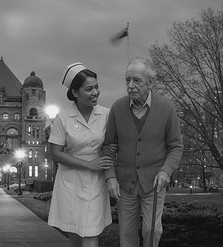  An elderly man walking with a nurse dressed in 1950s attire through modern-day Toronto; the black-and-white image blends pas