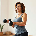 A 40 year old woman exercising with dumbbells in a simple, uncluttered space, looking focu