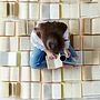 Woman reading book surrounded by numerous open books, holding coffee cup.