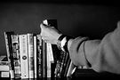 Hand reaching for a book on a dark, crowded bookshelf, black and white.