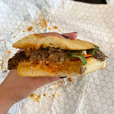 Hand holding a Tigerhawk sandwich filled with braised meat, sauce, and greens.