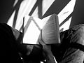 Person reading open book in strong sunlight with angular shadows, black and white.