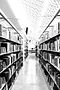 Narrow black and white library aisle filled with countless books.