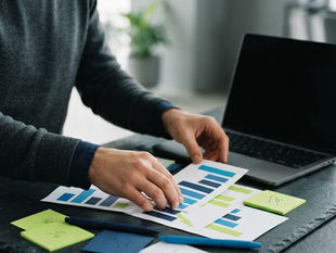 Hands organizing charts and notes on a desk to build a sales dashboard for small business growth tracking.